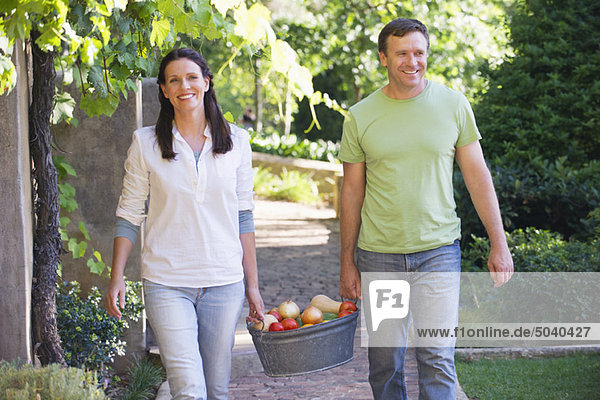Ein reifes Paar  das einen Früchtekorb im Garten trägt.