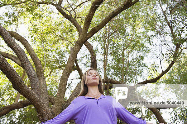 Junge Frau unter einem Baum stehend mit geschlossenen Augen