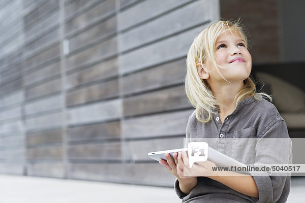 Mädchen hält ein digitales Tablett und schaut nach oben.