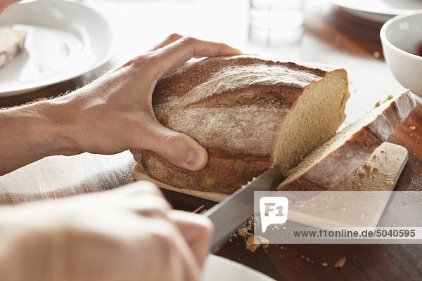 Nahaufnahme der Hand eines Menschen beim Brotschneiden