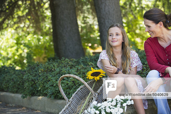 Kleines Mädchen und Mutter sitzend im Freien mit Blumen im Korb
