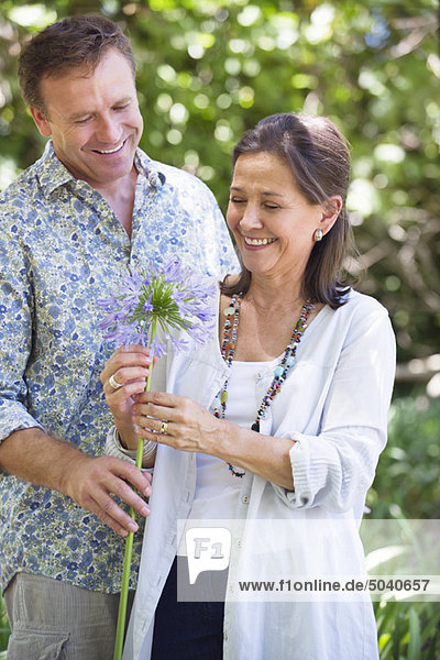 Ein Mann  der seiner Mutter eine Blume schenkt und lächelt.