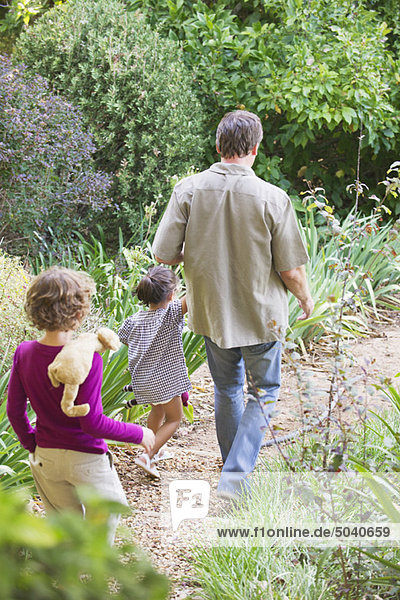 Vater mit zwei Kindern bei einem Spaziergang im Garten