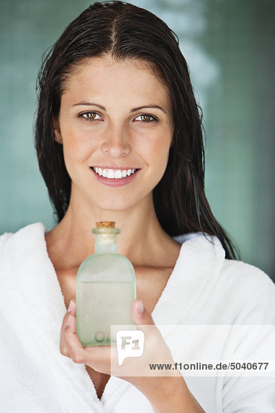 Porträt einer Frau  die eine Flasche Aromatherapieöl hält und lächelt.