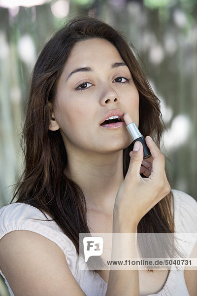 Portrait of a beautiful young woman applying lipstick