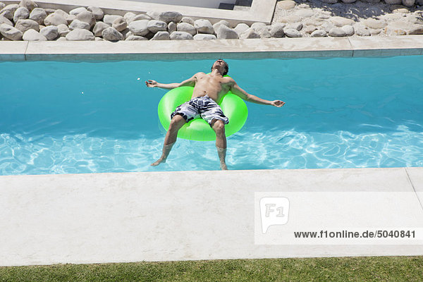 Mann entspannt auf einem aufblasbaren Ring im Pool