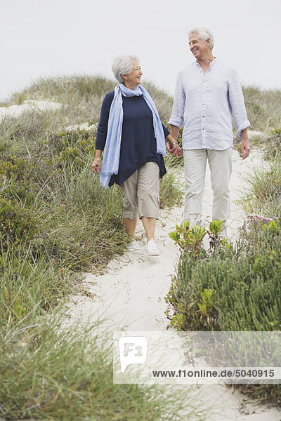 Seniorenpaar  das am Strand spazieren geht und sich an den Händen hält.