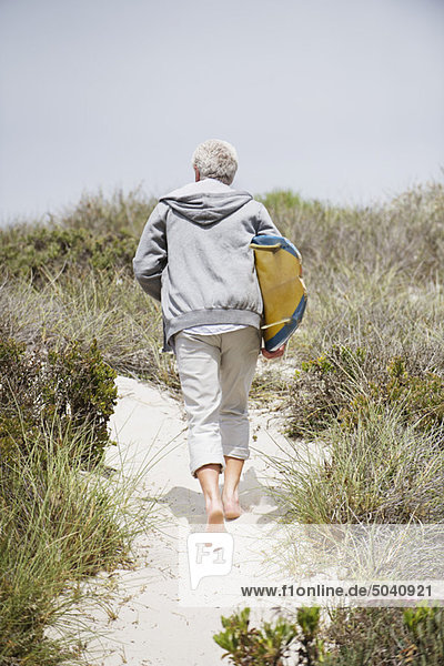 Rear view of a senior man carrying surfboard on the beach