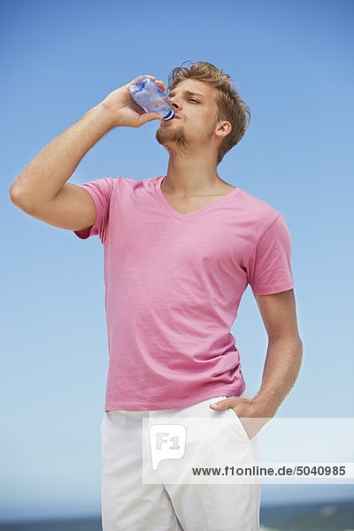 Junger Mann trinkt Wasser aus einer Wasserflasche am Strand
