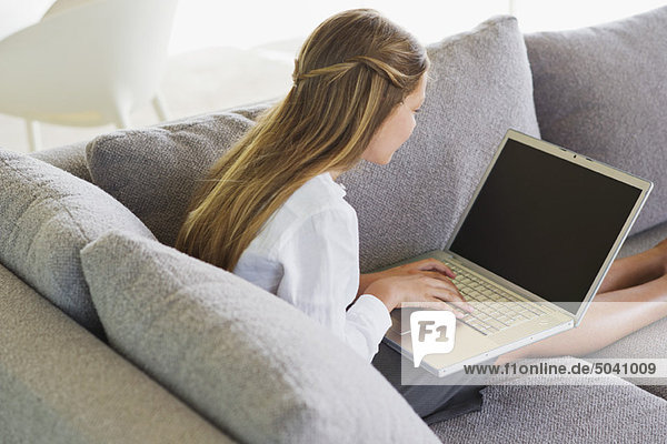 Seitenprofil eines Mädchens  das auf einer Couch sitzt und einen Laptop benutzt.