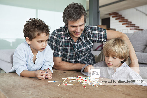 Boys playing pick up sticks with their father