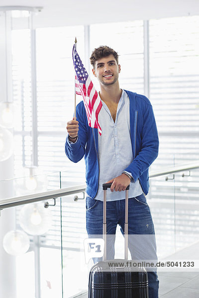 Porträt eines Mannes mit amerikanischer Flagge und Koffer am Flughafen