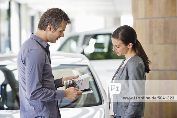 Side profile of a couple looking at catalog in car showroom