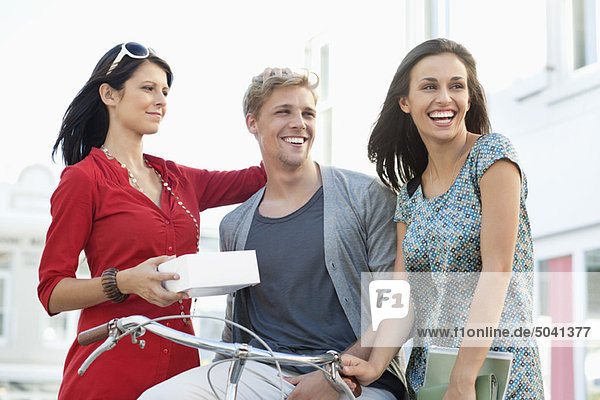 Lächelnder junger Mann mit zwei Frauen beim Radfahren
