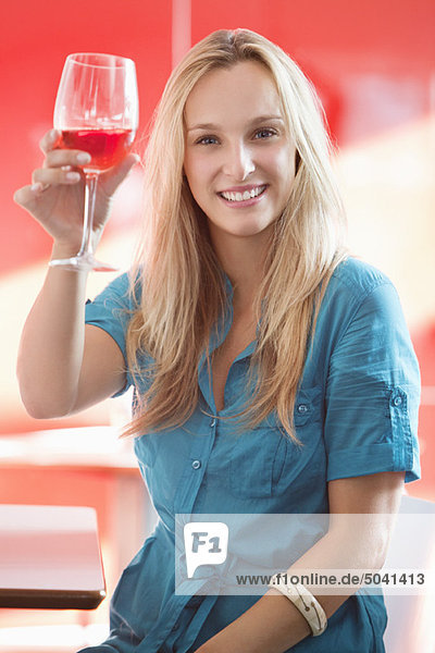 Junge Frau röstet Weinglas und lächelt in einer Bar
