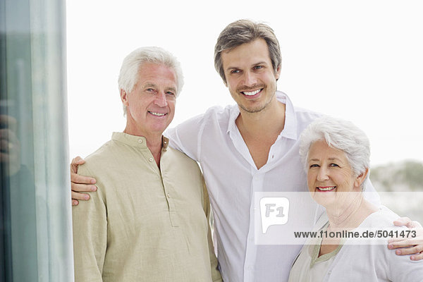 Porträt eines erwachsenen Mannes,  der mit den Armen zu seinen Eltern steht.
