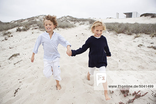 Boy with his sister holding hands and running on sand