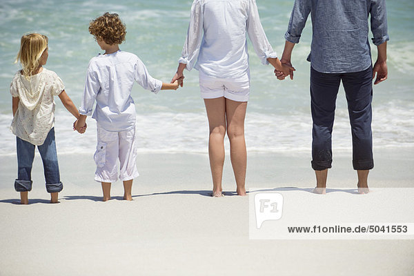 Paar mit zwei Kindern am Strand stehend