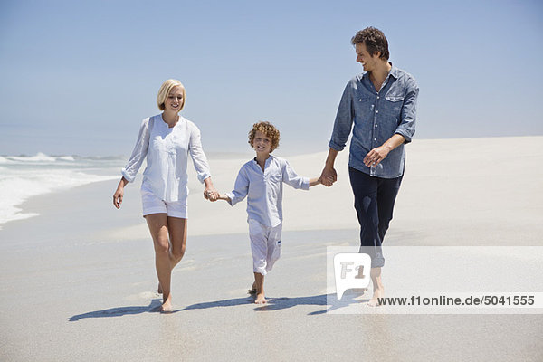Ein Paar  das mit seinem Sohn am Strand spazieren geht.