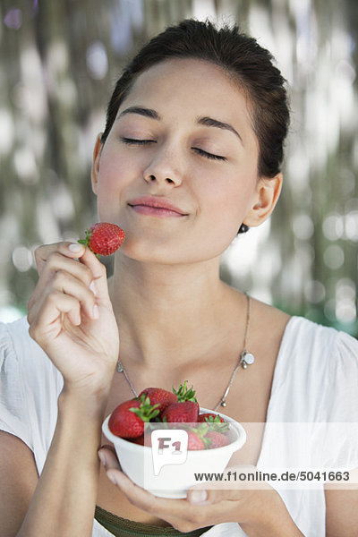 Schöne junge Frau hält eine Schale Erdbeeren mit geschlossenen Augen.