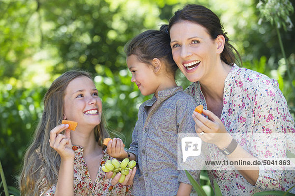 Glückliche Mutter isst Früchte mit ihren beiden Töchtern im Freien.