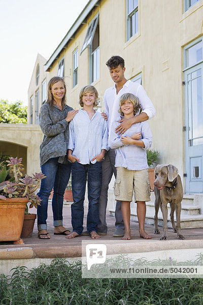 Porträt einer Familie  die mit ihrem Hund vor dem Haus steht.