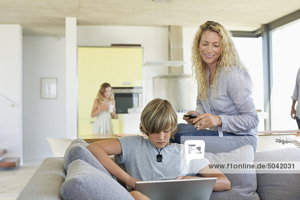 Teenager-Junge  der einen Laptop benutzt und seine Mutter  die ihn ansieht.