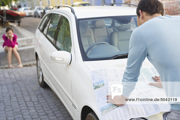 Rear view of a man looking at map on car with young woman sitting in the background