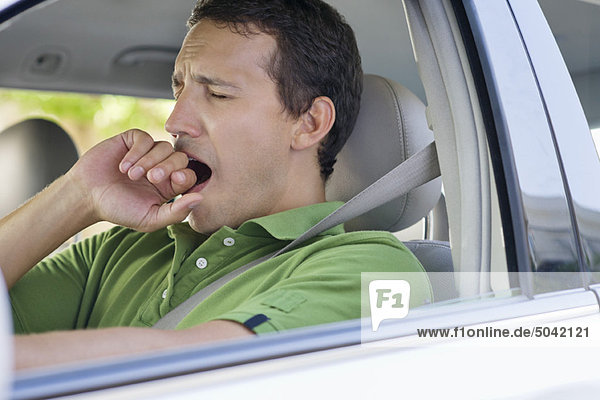 Mid adult man yawning while driving a car