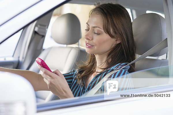 Schöne junge Frau mit dem Handy beim Autofahren