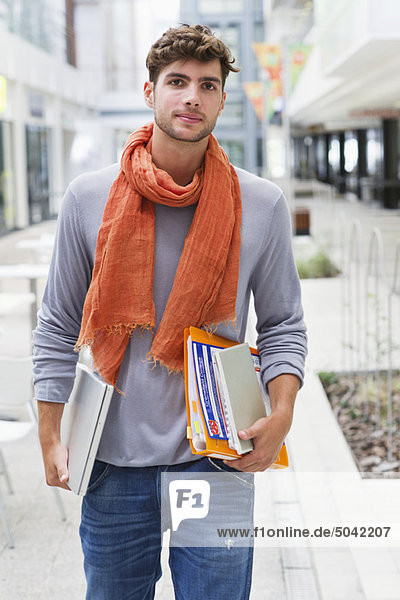 Porträt eines Mannes  der mit Büchern und einem Laptop in der Hand geht.