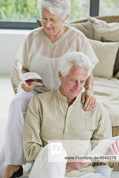 Ein älterer Mann arbeitet an einem digitalen Tablett und seine Frau liest eine Zeitschrift.
