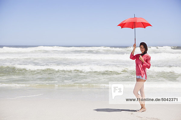 Frau am Strand stehend mit Schirm