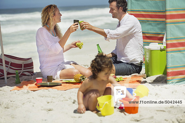 Ein paar Toasts mit einem Drink  während ihre Tochter am Strand spielt.