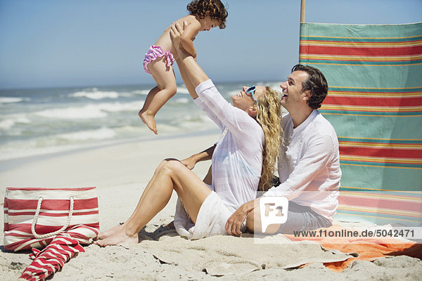 Ein Paar spielt mit seiner Tochter am Strand.