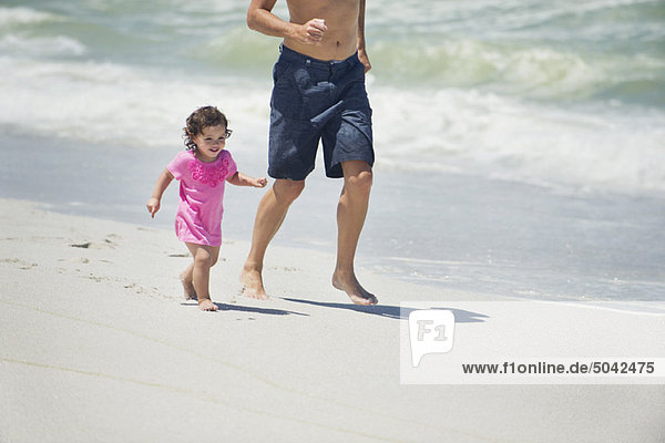 Mann läuft mit kleiner Tochter am Strand.