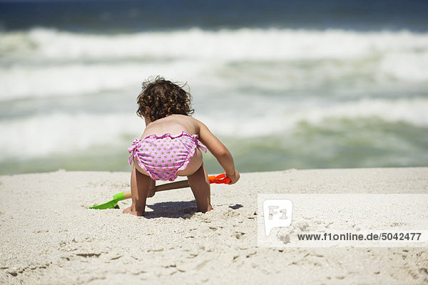 Rear view of a girl digging with a sand shovel on the beach
