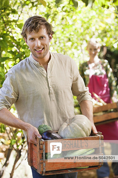 Lächelnder Mann hält eine Kiste mit Gemüse.