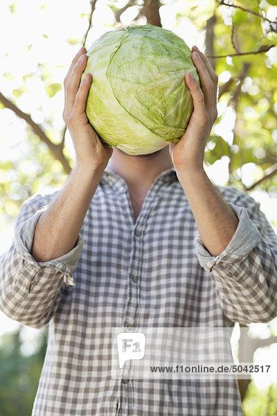Man holding a cabbage in front of his face