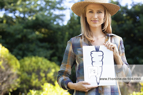 Portrait of a young woman showing carrot painting in a field