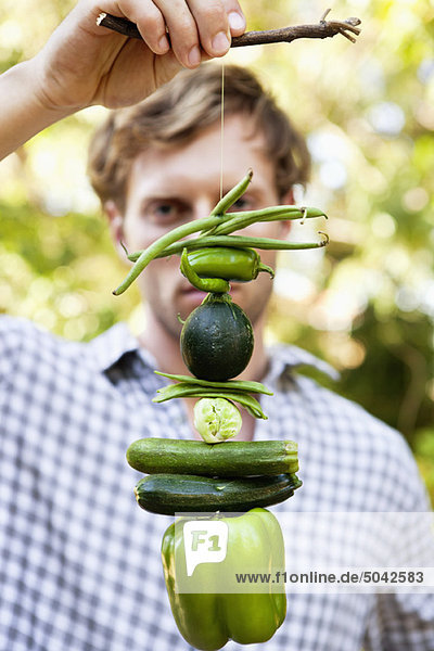 Man holding vegetables hanging on a twig