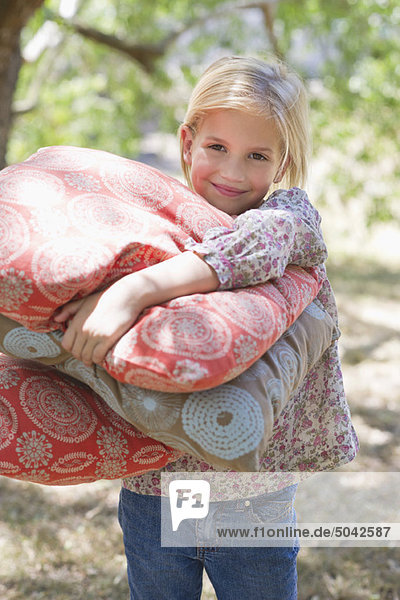 Portrait of a smiling little girl carrying pillows outdoors