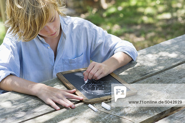 Little boy making drawing of tree on slate outdoors