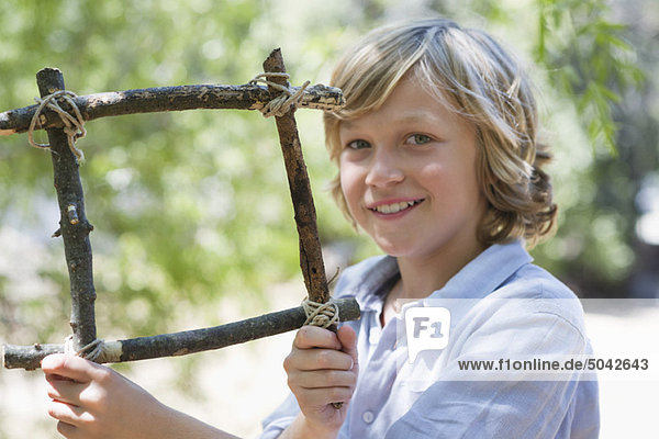 Portrait of a cute little boy holding frame of driftwood outdoors