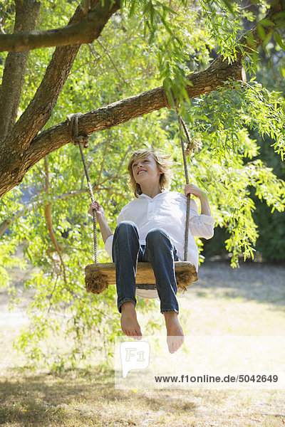 Happy little boy swinging on tree