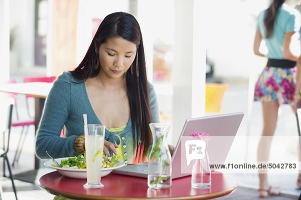 Beautiful woman eating food with laptop on table in a restaurant