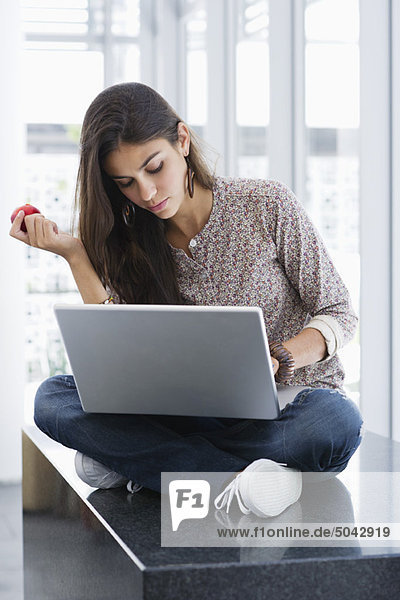 Schöne Frau  die einen Apfel hält  während sie einen Laptop benutzt.