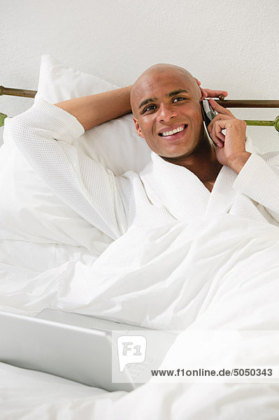 Man in bed with laptop and cellphone