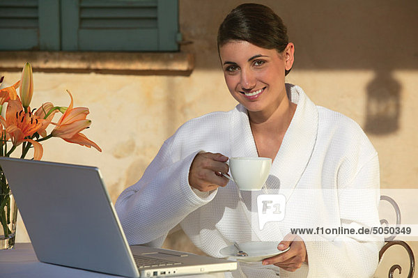 Frau im Bademantel mit Kaffee und Laptop