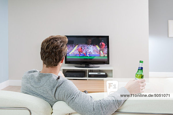 Junger Mann beim Fußball im Fernsehen mit Bierflasche